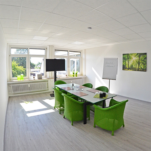 Besprechungsraum mit Monitor, Tisch und grünen Stühlen in einem Büro