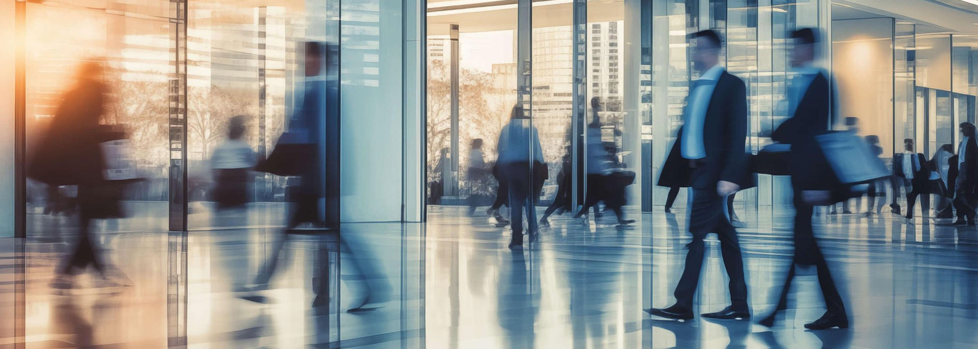 KI in Unternehmen – Beispiele Dieses Bild zeigt geschäftige Menschen in Business-Kleidung, die sich schnell durch eine moderne Bürolobby mit großen Glasfronten bewegen.