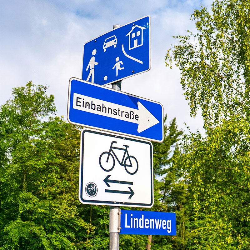 Mehrere blaue Straßenschilder untereinander vor einem Wald