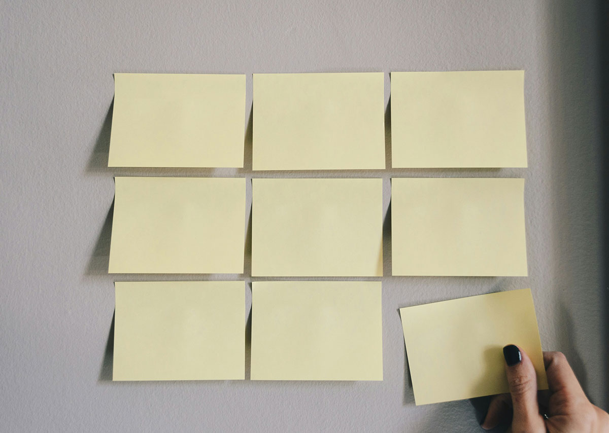 Welche Maßnahmen gehören zum Inbound Marketing? Mehrere gelbe Post-its werden von einer Hand an eine graue Wand geklebt