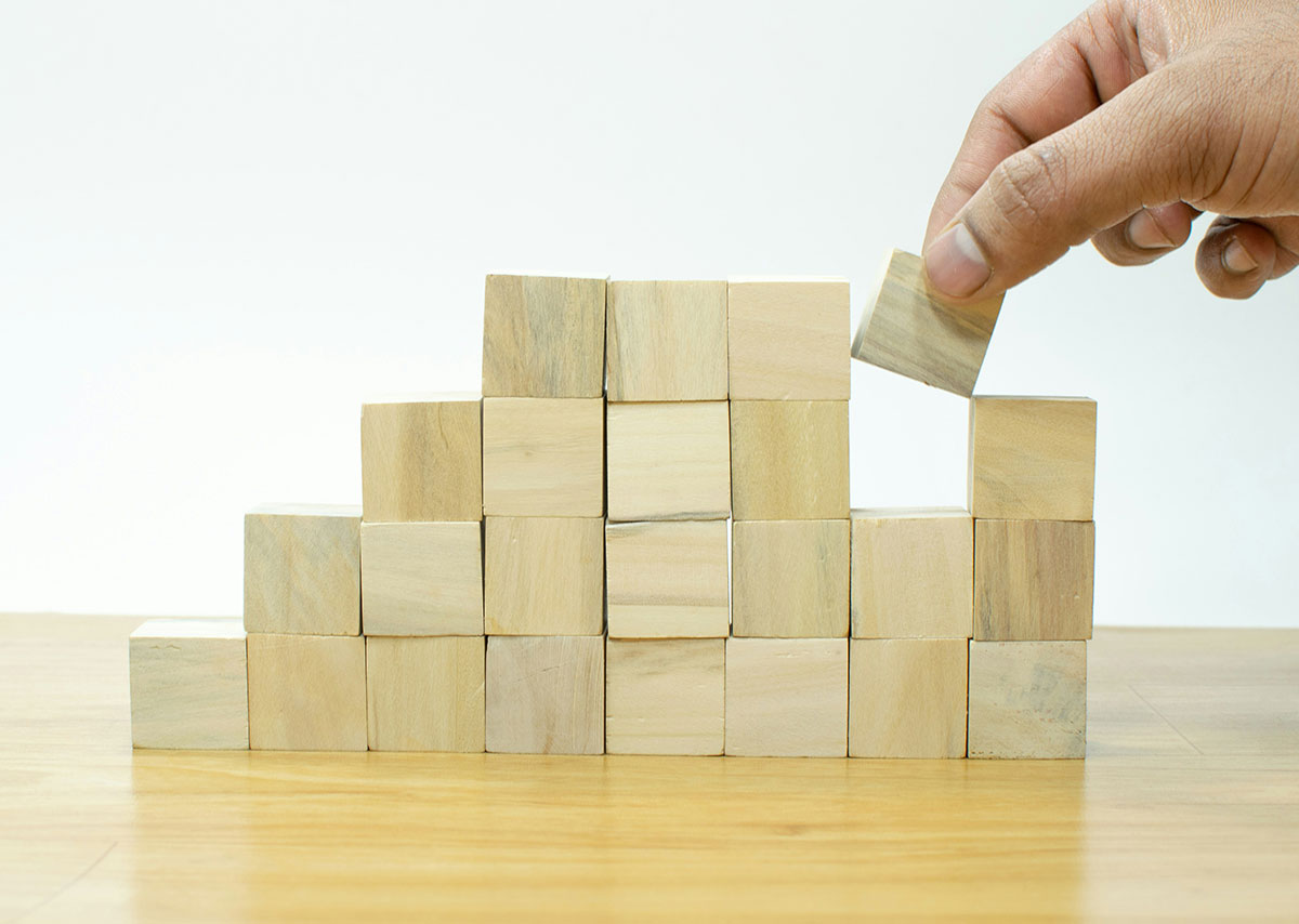 Large Language Model Optimization (LLMO) Eine Hand setzt einen einzelnen Holzbaustein in ein bestehendes Gebilde aus Holzbausteine