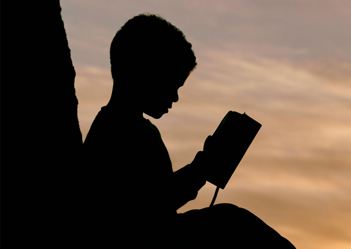 LLM-Readability Dieses Foto zeigt die Silhouette eines Kindes, das während des Sonnenuntergangs liest.