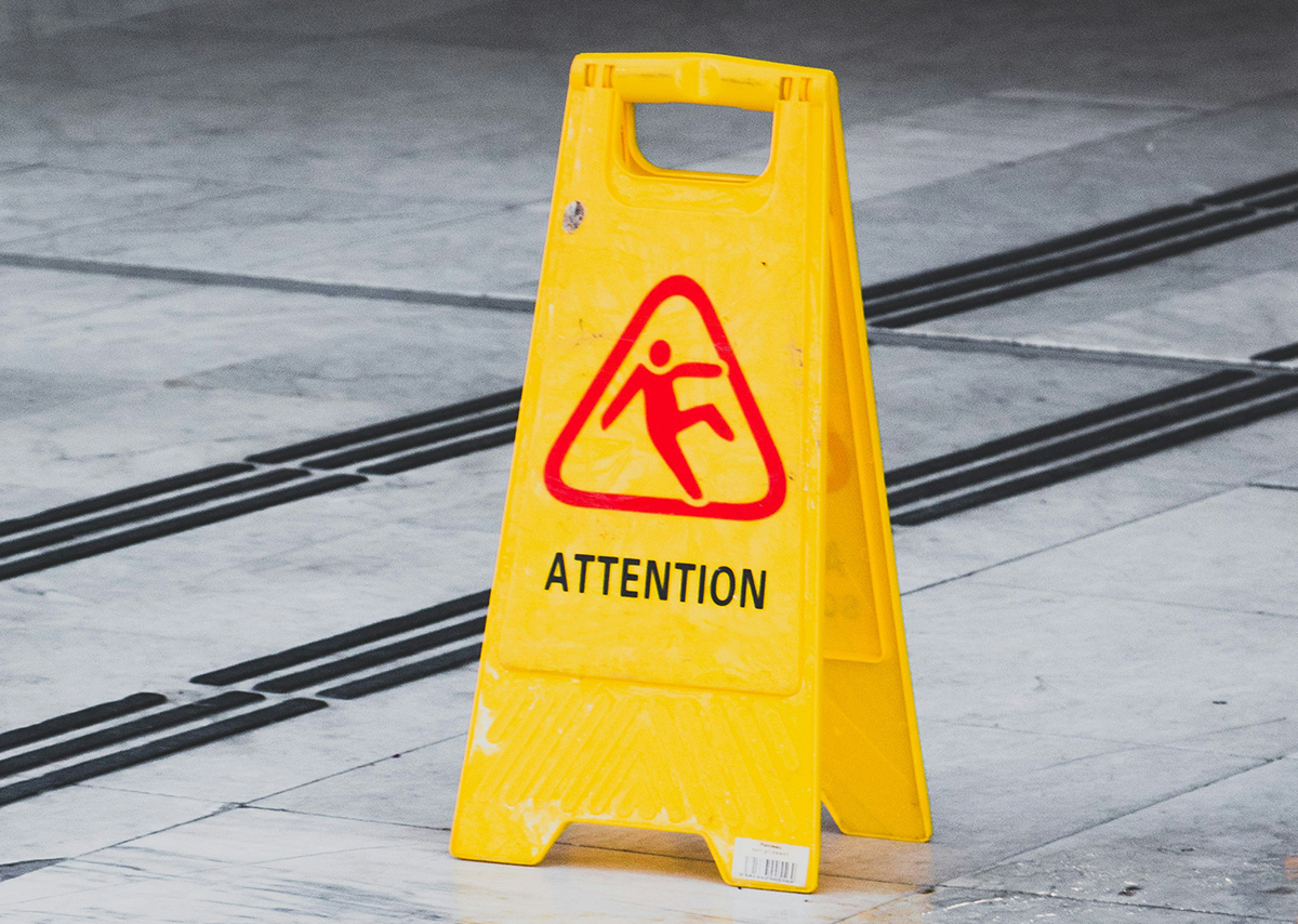 Dies ist ein gelbes Warnschild mit der Aufschrift „Attention“ und einem Piktogramm für Rutschgefahr.