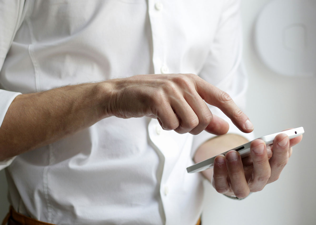 Eine Person in weißem Hemd tippt auf sein Smartphone