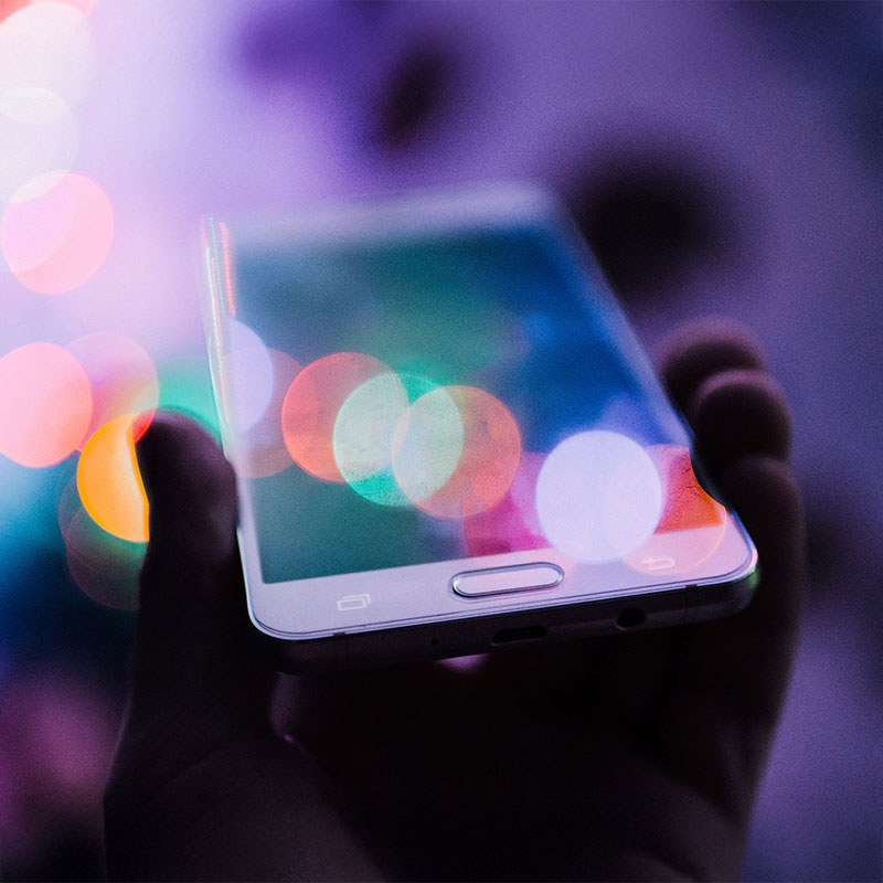 Eine Hand hält ein Handy auf dem Display spiegeln sich mehrere Farben