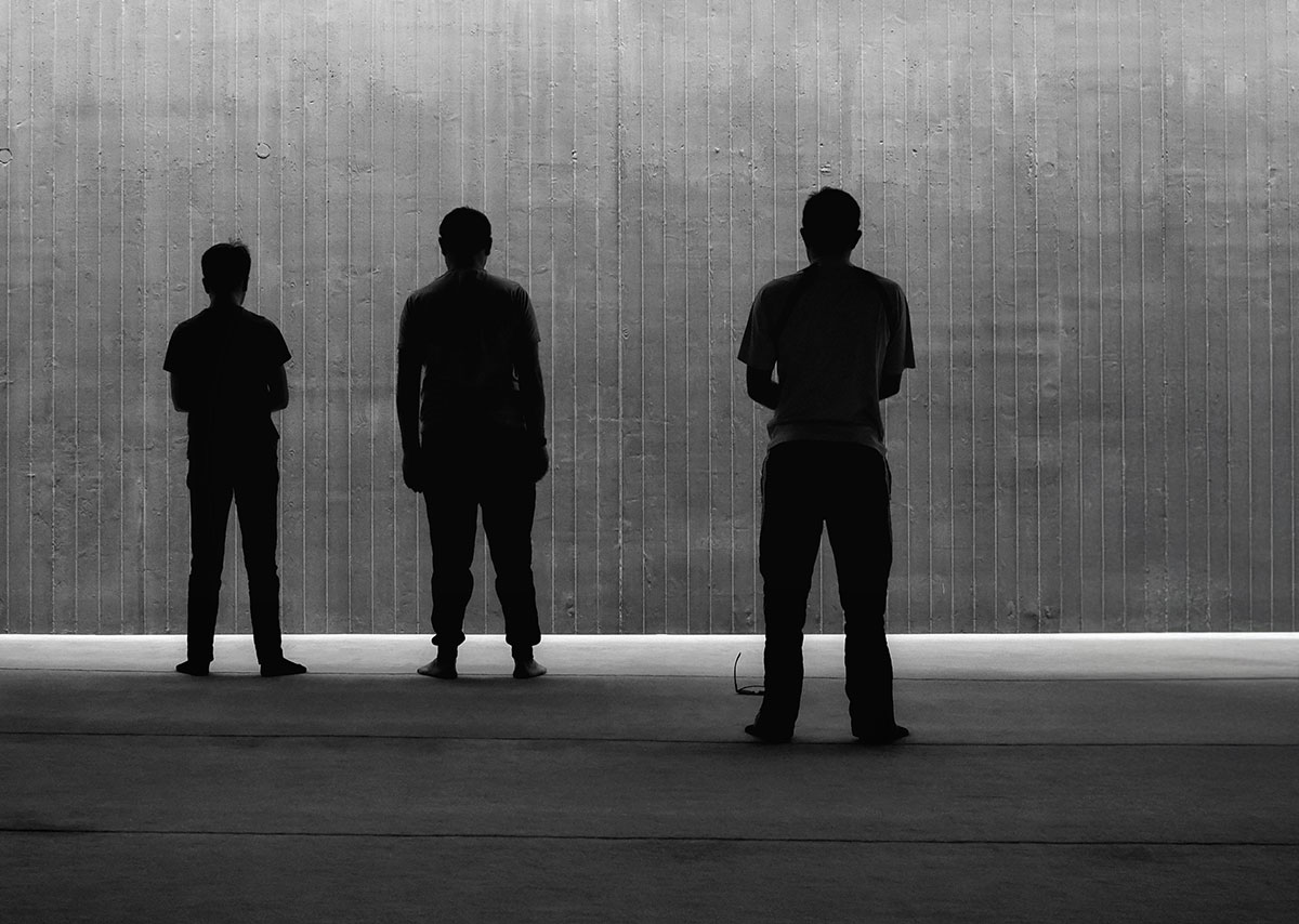 3 Silhouetten von Personen vor einer grauen Wand