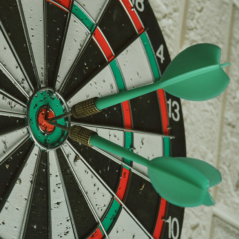 Eine Dartscheibe, in der zwei grüne Dartpfeile in der Mitte stecken