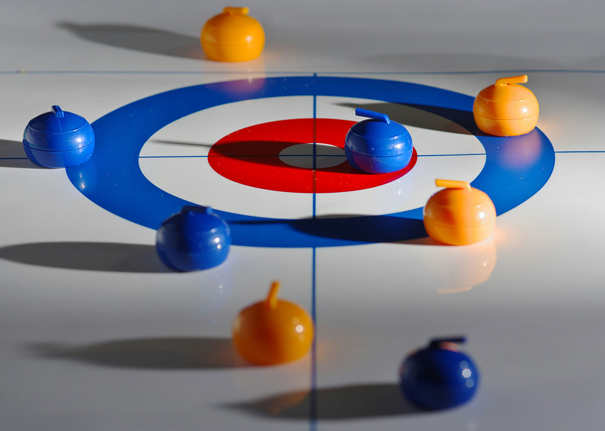 Ein Curling-Spiel mit blauen und orangenen Curlingstein