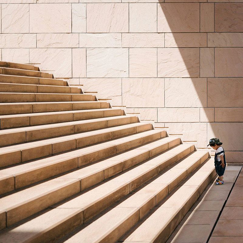 Kleinkind steht vor beigefarbener Betontreppe