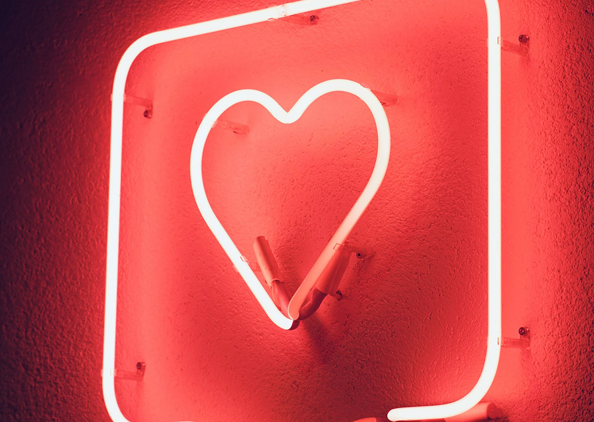 Social Sight und Social Media Marketing Das Bild zeigt eine rote Leuchtreklame in Form eines leuchtenden Herzens vor einer strukturierten Wand.